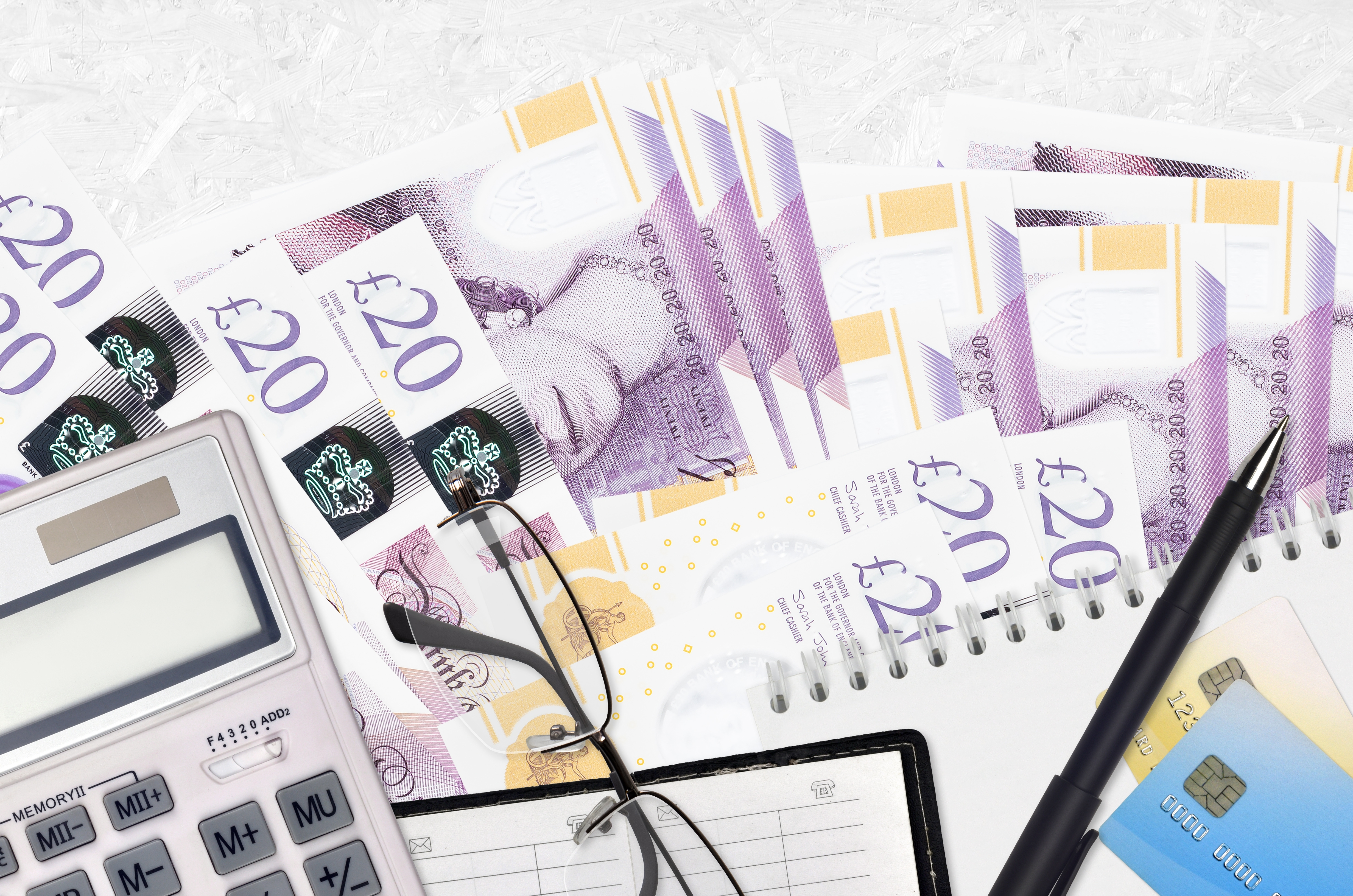 An image of 20 pound notes, a calcuator, reading glasses and a pen