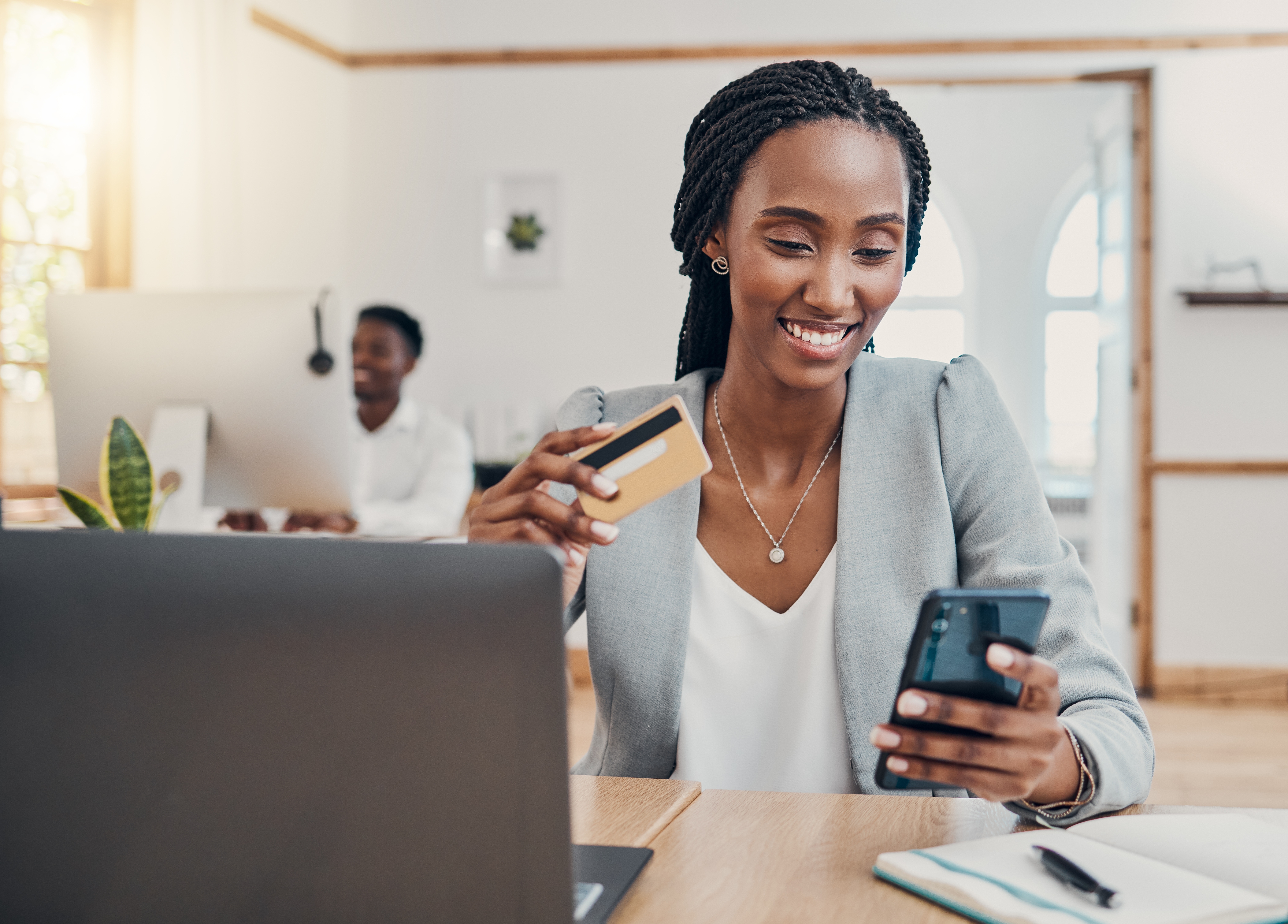 A woman holding a mobile device and a credit card at her office desk